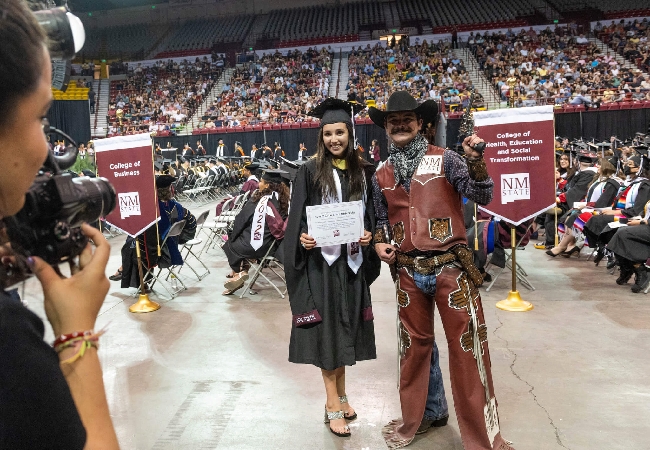 An NMSU graduate is posing with the school mascot, Pistol Pete, during commencement.