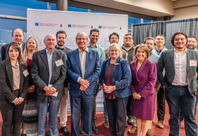 The CFR group stands together in front of a banner at an NMSU alumni event.